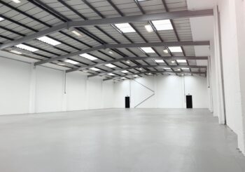 An empty, newly renovated industrial warehouse with pristine white walls and a clean, polished concrete floor, illustrating the final stage of the industrial fit-out process